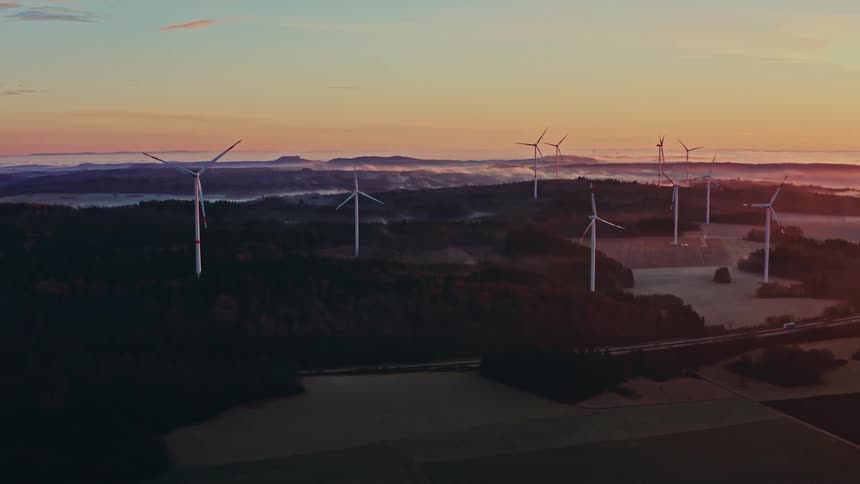 A windmill stands in the countryside at sundown with a freeway running beside it as cars drive past under the warm glow of the setting sun