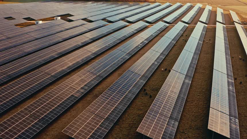 Sunlight shines on solar panels lined up across the ground