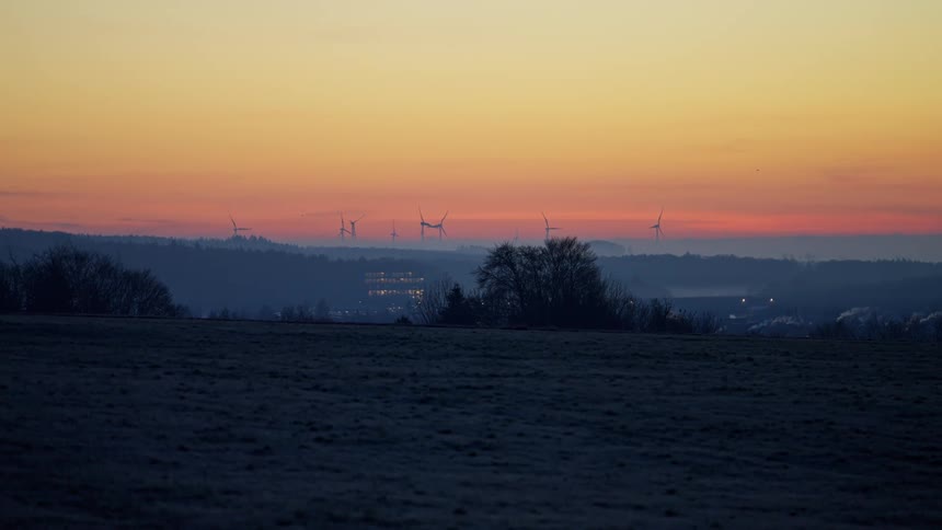 Wind turbines appear on the horizon beneath a dawncolored sky over open fields