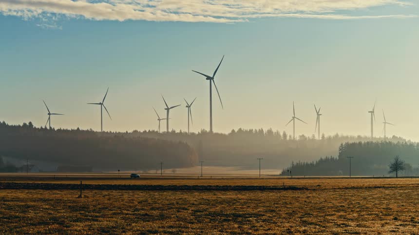 Turbines spinning on a wind farm as traffic moves on the road
