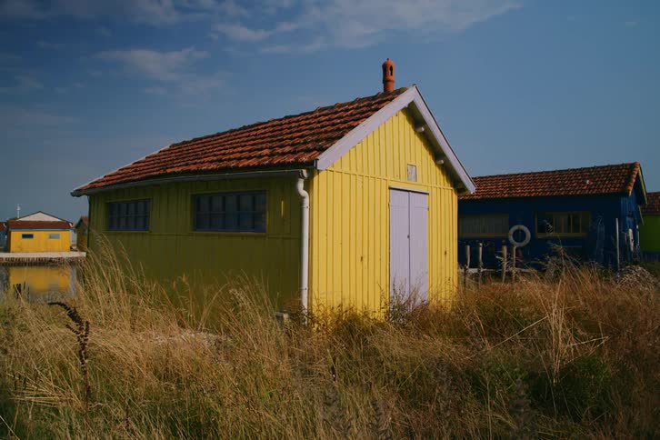 A colorful yellow cabin sits in tall dry grass beneath a clear blue sky