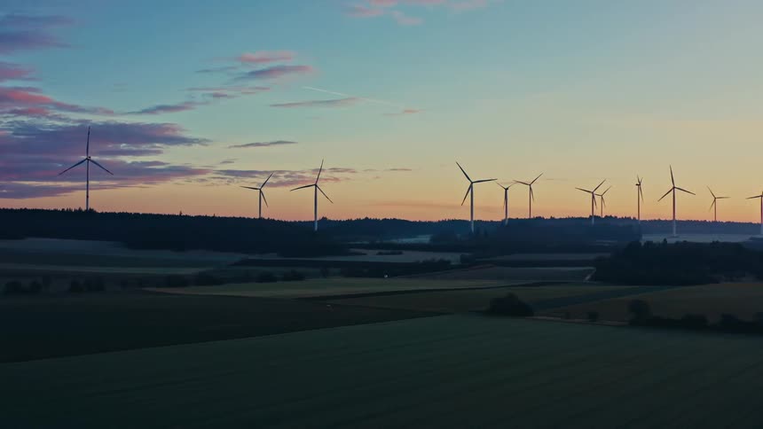 Wind turbines on a field with hills on the background outdoors during dusk or dawn