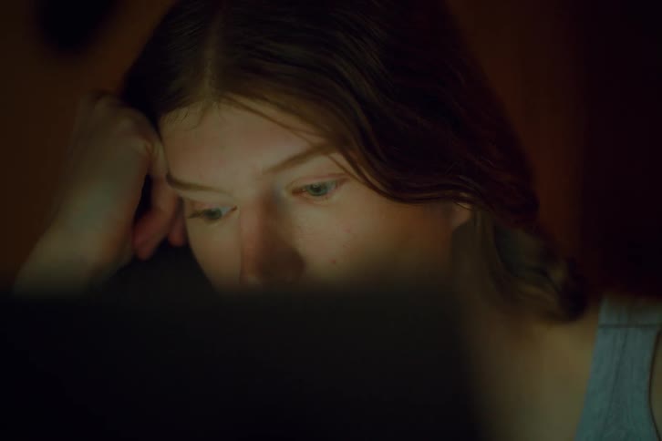 The brown haired woman is staring at a laptop screen while resting her head on her hand4