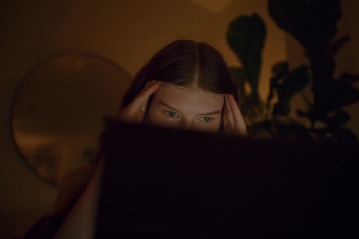 Woman using a laptop in a dimly lit room rubs her temples
