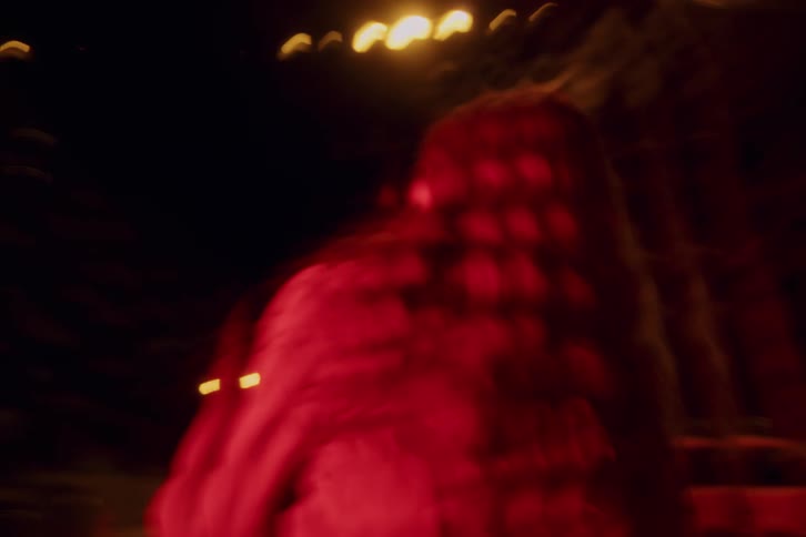 Person standing under red and blue lights in nighttime setting with illuminated urban elements