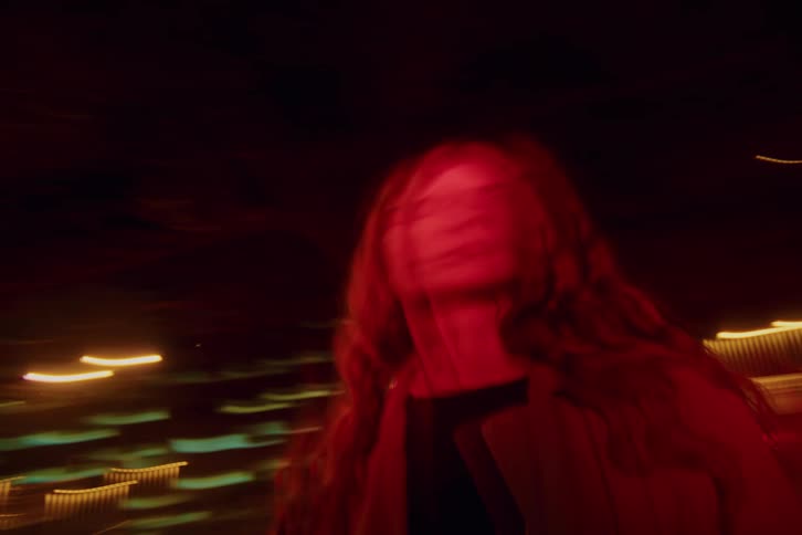 Androgynous person wearing a coat standing on a street on a metropolitan area outdoors during night time