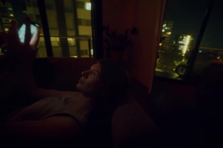 Woman lying on the sofa at night interacting with a smartphone
