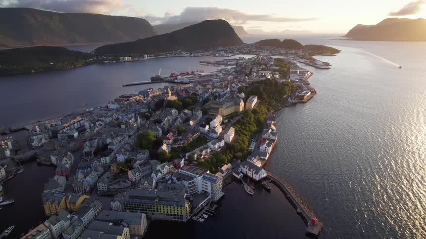 Aerial view of a coastal town nestled between mountains and water glows under the sunset sky