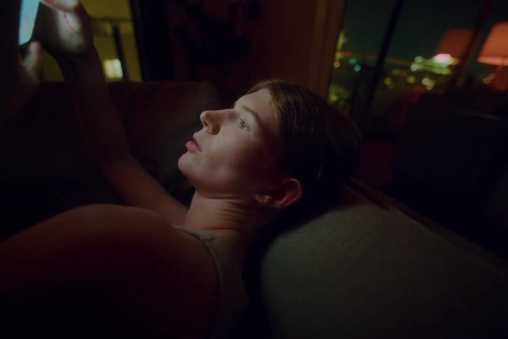A woman sits on the couch while texting on her cell phone