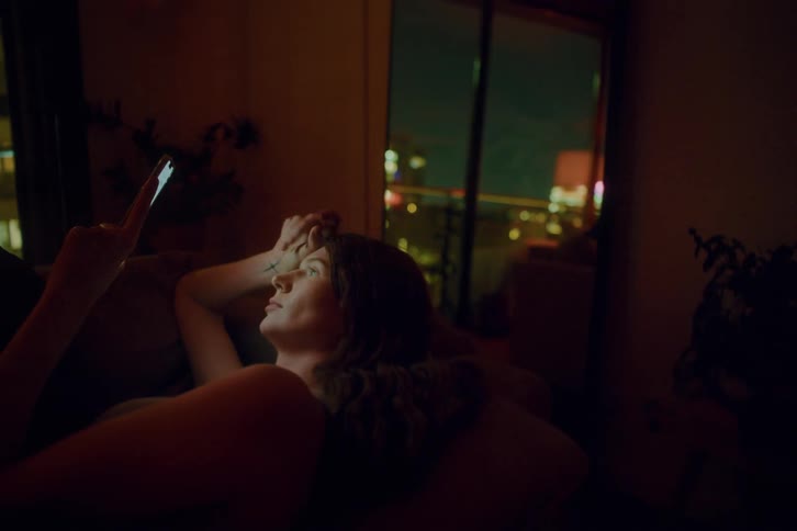The woman laying on her couch is looking at her phone