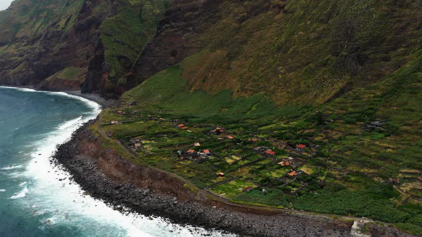 A small coastal town sits along the shoreline at midday with a mountain rising in the background