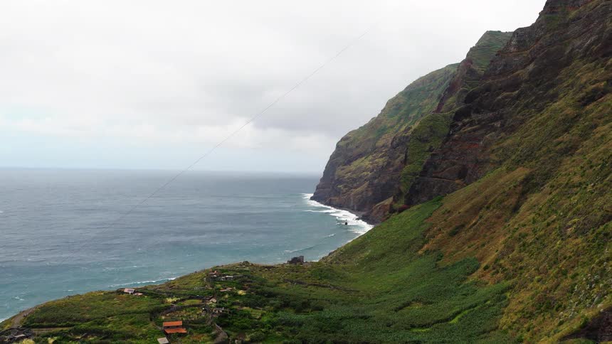 Aerial wide view of green cliffs and a coastal village beside the ocean under cloudy sky