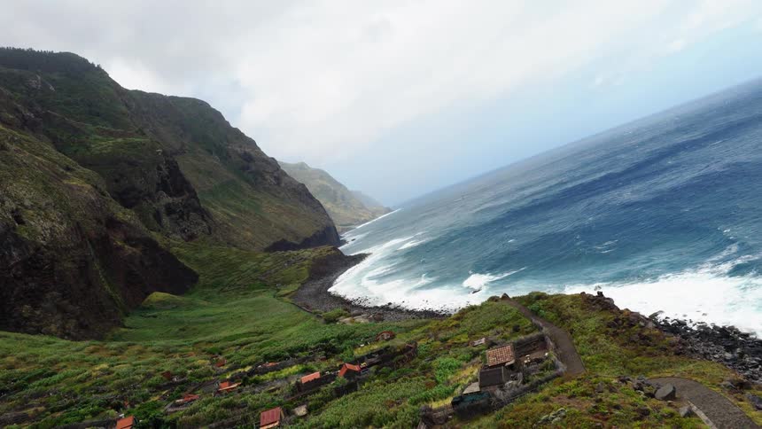 Green cliff with scattered houses follows a rocky coastline beside the ocean