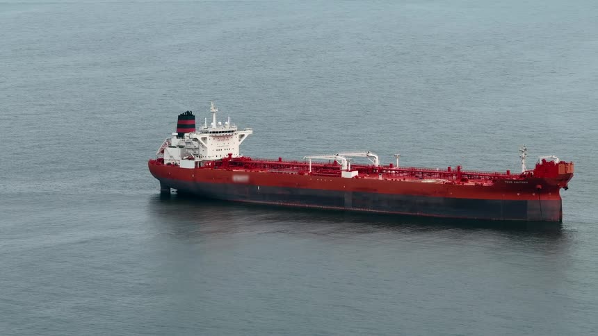 A large red and black ship floats stationary on the dark grey surface of the open sea