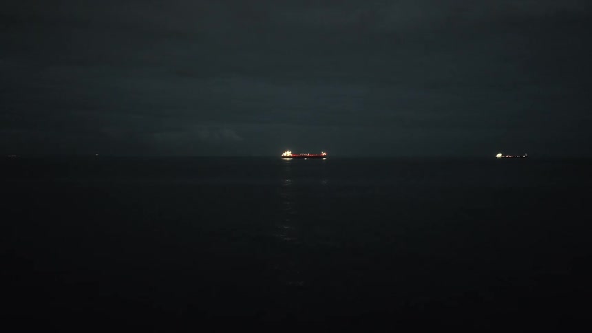 Two boats riding on the ocean at night as waves roll toward the shore