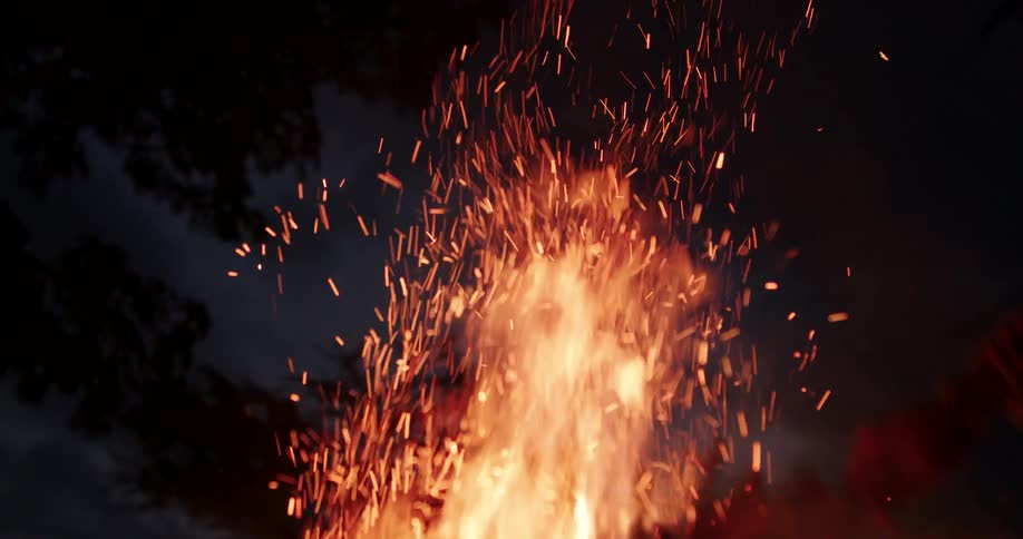 Human hand shaking a branch on fire outdoors during night time