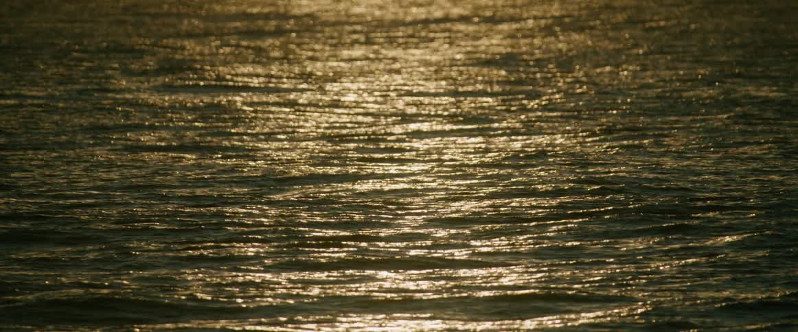 Golden sunlight reflects off the rhythmic ripples of the ocean surface at sunset creating a shimmering texture of light and shadow across the moving water as small waves flow
