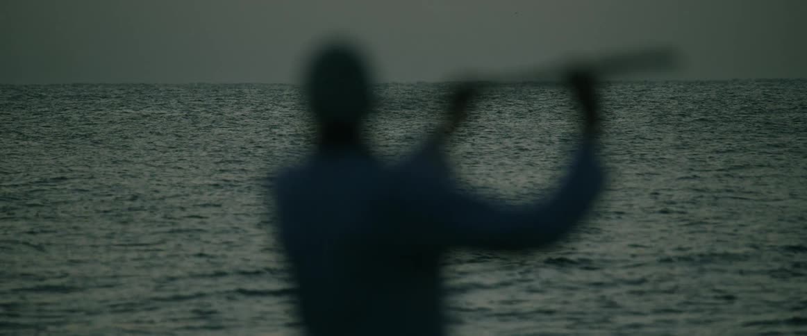 Blurred silhouette of a person raises an object in front of the sea at dusk