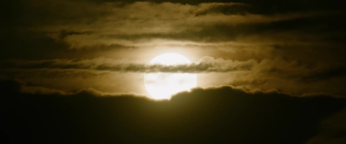 Bright astronomical object shines in an amber tinted sky casting clouds into silhouette