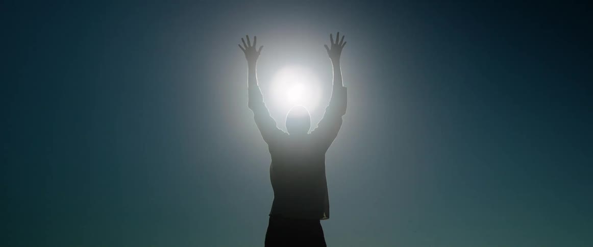 Person opening their arms against a blue sky with the sun prominently displayed