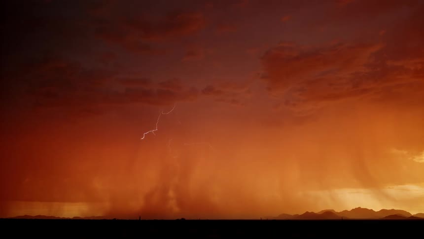 Lightning illuminates storm clouds over a dark landscape beneath an orange sky