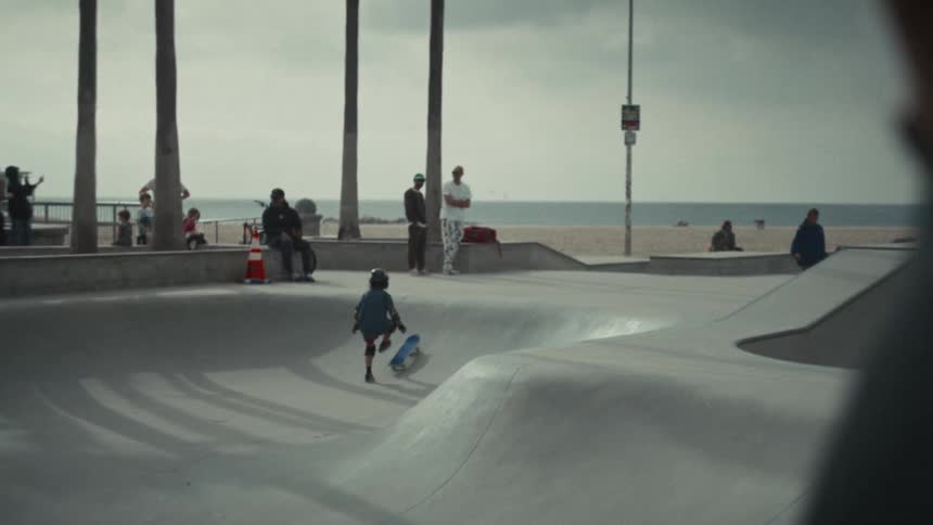 Boy performing a skateboarding trick on an outdoor skate park with a beach in the background