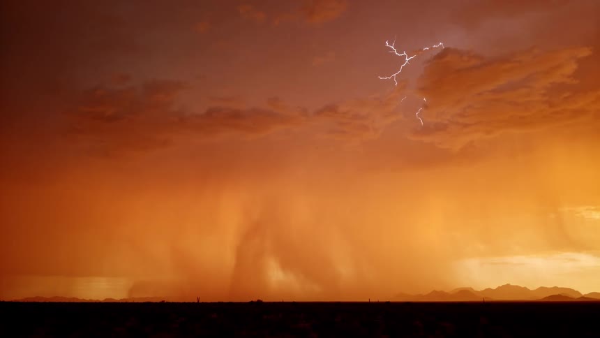 Dramatic lightning splits an orange sky over dark mountains during a fierce storm