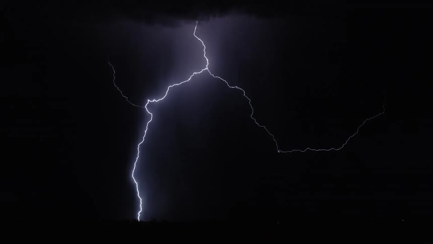 White lightning bolt striking ground during nighttime storm with dark sky and lit clouds