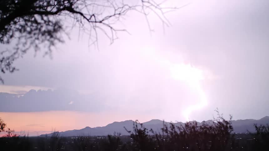 Lightning streaks across the night sky over a mountain silhouette lit by sunset