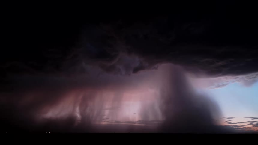 A wide view of a heavy curtain of rain falling from dark storm clouds over a flat horizon at twilight