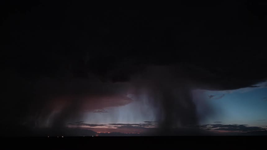 Lightning pierces dense clouds with visible rain shaft in the background during evening storm