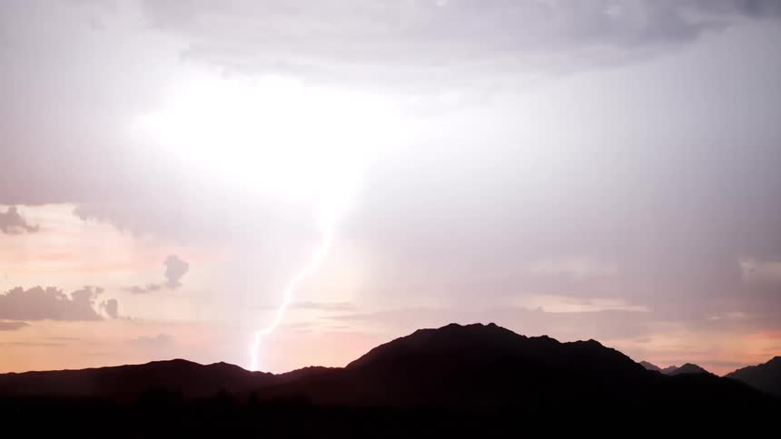Lightning appears among dark clouds above a mountain silhouette at sunset