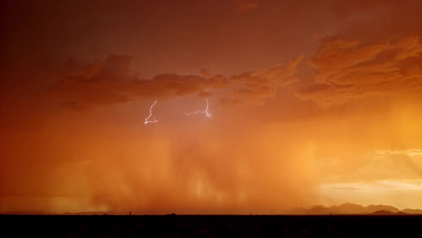 A cloudy orange sky glows with warm stormy light as a bolt of lightning strikes beneath the thick clouds illuminating the horizon with a sudden electric flash