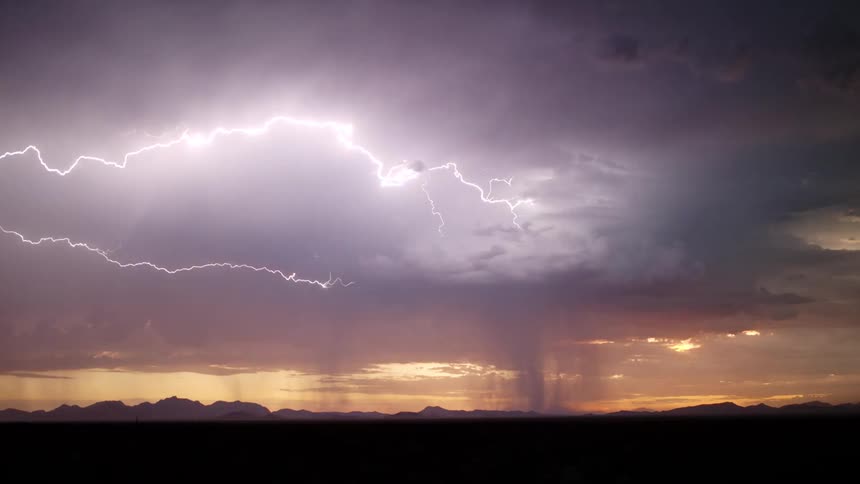 Thunders and lightning among dark clouds in a thunderstorm on the sky over a field with mountains on the background outdoors during dusk or dawn