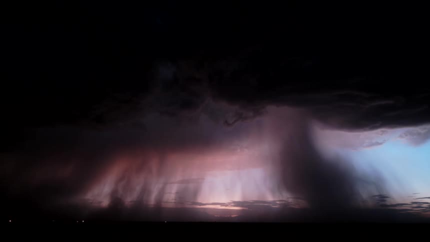 As a powerful storm cell forms at dusk flashes of lightning illuminate the churning clouds and sheets of rain from within