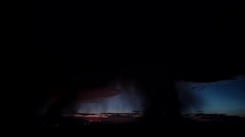 A powerful lightning bolt strikes vertically from dark storm clouds during a night tempest illuminating heavy rain shafts and a flat horizon line as the surrounding sky transitions from deep blue to pitch black