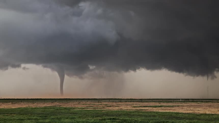 A large tornado touches down in an open field beneath a dark stormy sky