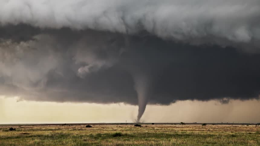 Dark cloud fills the sky as a tornado spins across rural land