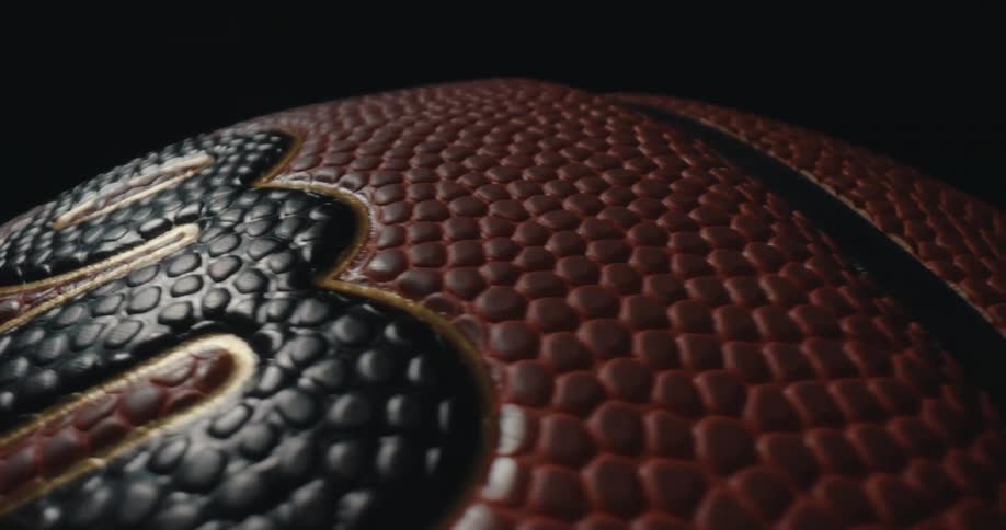 A soccer ball on a field at night illuminated by bright light that highlights its red and black textured surface