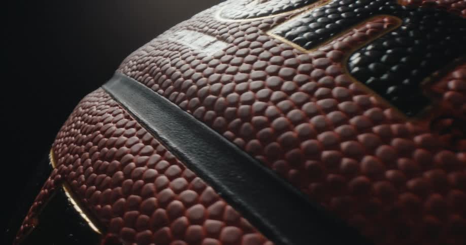A close view of the textured surface of a basketball shows the orange pebbled leather and black rubber ribs as the ball rotates slowly under a single light source