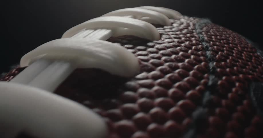 An extreme closeup shows an american football rotating slowly against a black background