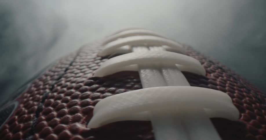 Leather texture with white stitching highlighted on american football against smoky background