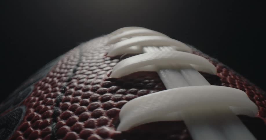 A close up view of a wilson american football showing its textured surface and white laces against a dark background