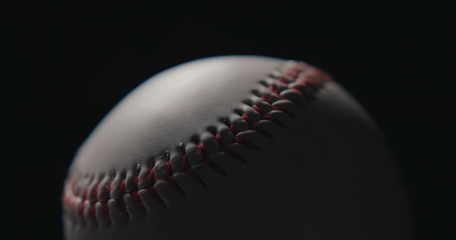 Baseball in closeup with red stitching highlighted against a dark background