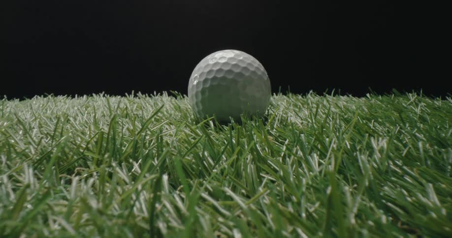A lowangle view pushes through blades of lush green grass to reveal a white golf ball sitting expectantly against a clean black background