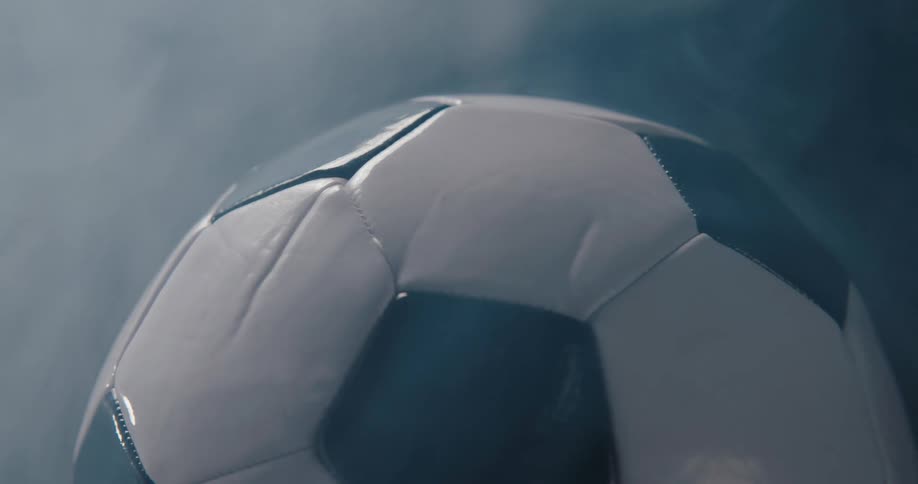 Light shines on a soccer ball as it turns and rotates as smoke rises