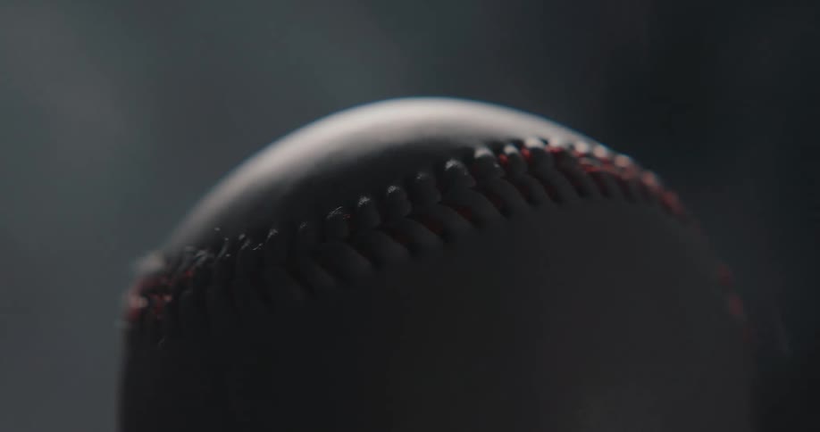 Close up of a white baseball surrounded by vapour in a dark photo studio