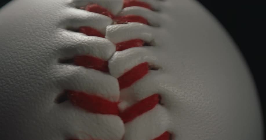 Red stitching runs across white leather surface of baseball
