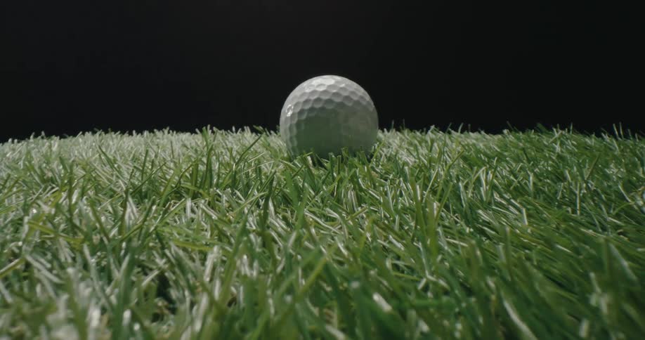 White golf ball rests on green turf against dark background