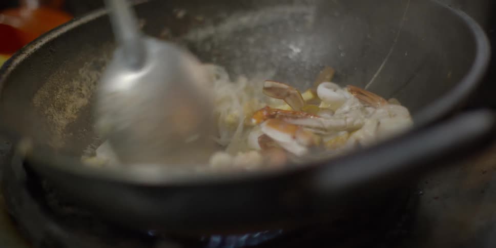 Noodles and mushrooms being stirred and cooking in a pan